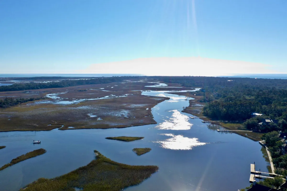 A panoramic view of river and marshland with distant trees and a small boat, offering a glimpse of the serene waterways and natural habitats that define the island’s landscape. The expansive view encourages thoughts of boating, birdwatching, and quiet nature walks.