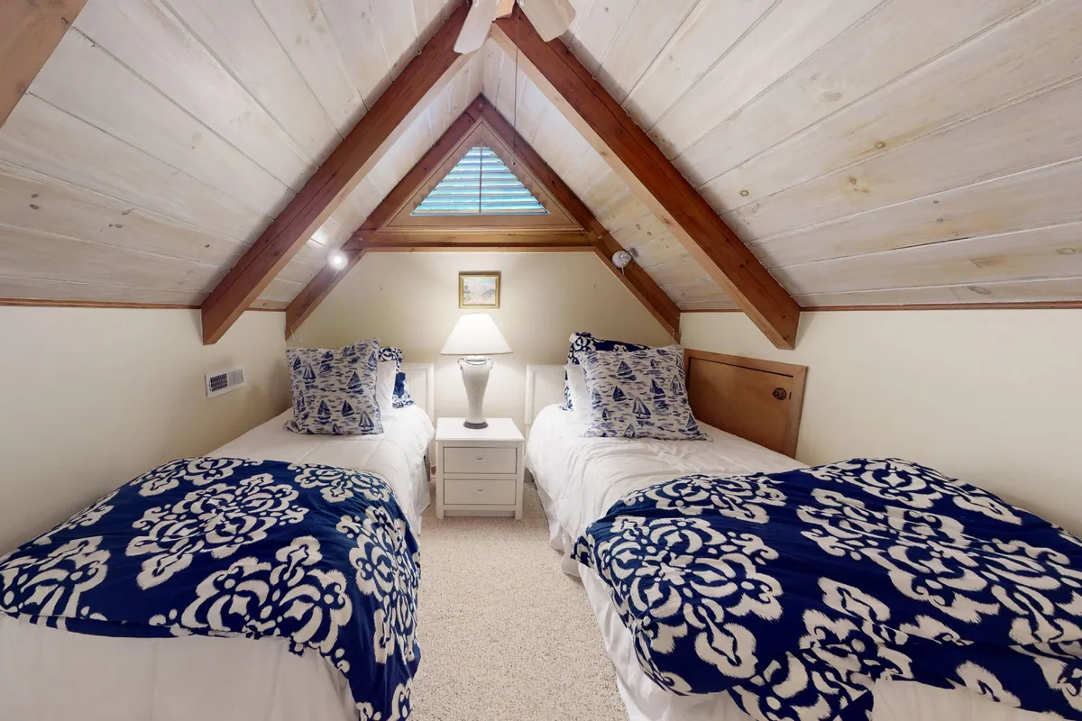 A cozy loft or bedroom area featuring twin beds, a table lamp, and decorative wall art. The setting is relaxed, perfect for children or teens, with space for reading or late-night chats.
