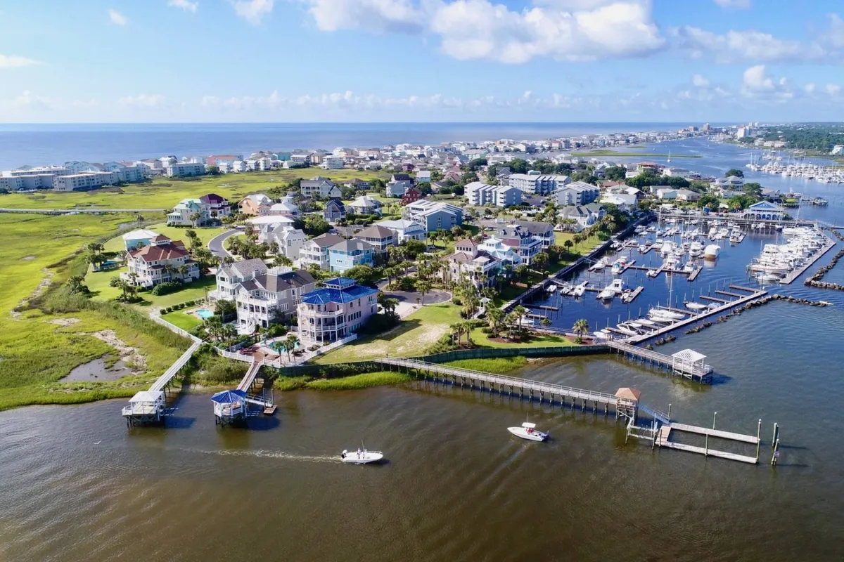 A panoramic view of waterfront homes, a marina dotted with boats, vibrant green landscapes, and the sparkling blue ocean. The scene invites exploration and highlights the vibrant community atmosphere.