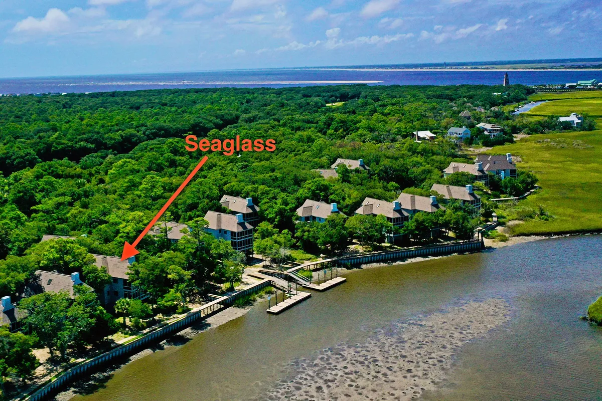 A tranquil waterfront scene featuring the Seaglass property surrounded by lush greenery, with a dock extending over calm water. The nearby lighthouse adds a sense of place, and the area invites activities such as boating, fishing, and relaxing by the water.