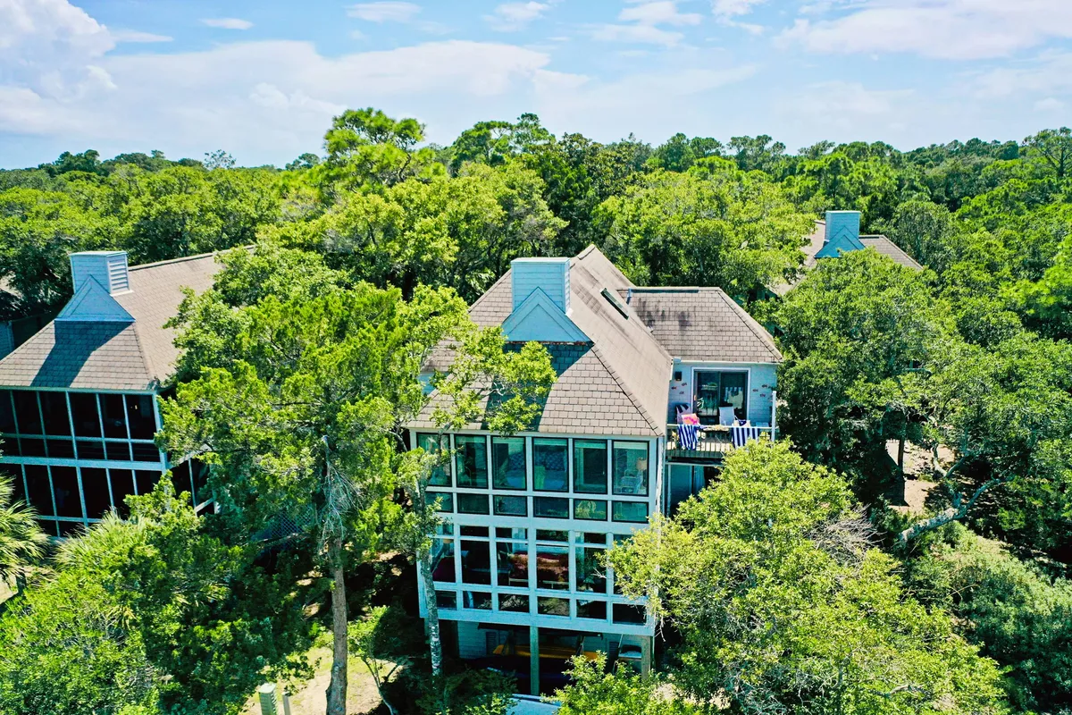 An exterior shot of the house, nestled among mature trees, with a balcony furnished for relaxation. The natural setting hints at easy access to outdoor activities and tranquil spots to unwind after an active day.