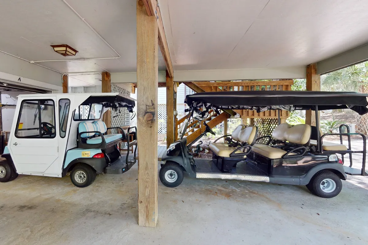 An interior view of two golf carts parked indoors beside wooden support beams and stairs, illustrating the convenience of in-island travel options provided with the property.