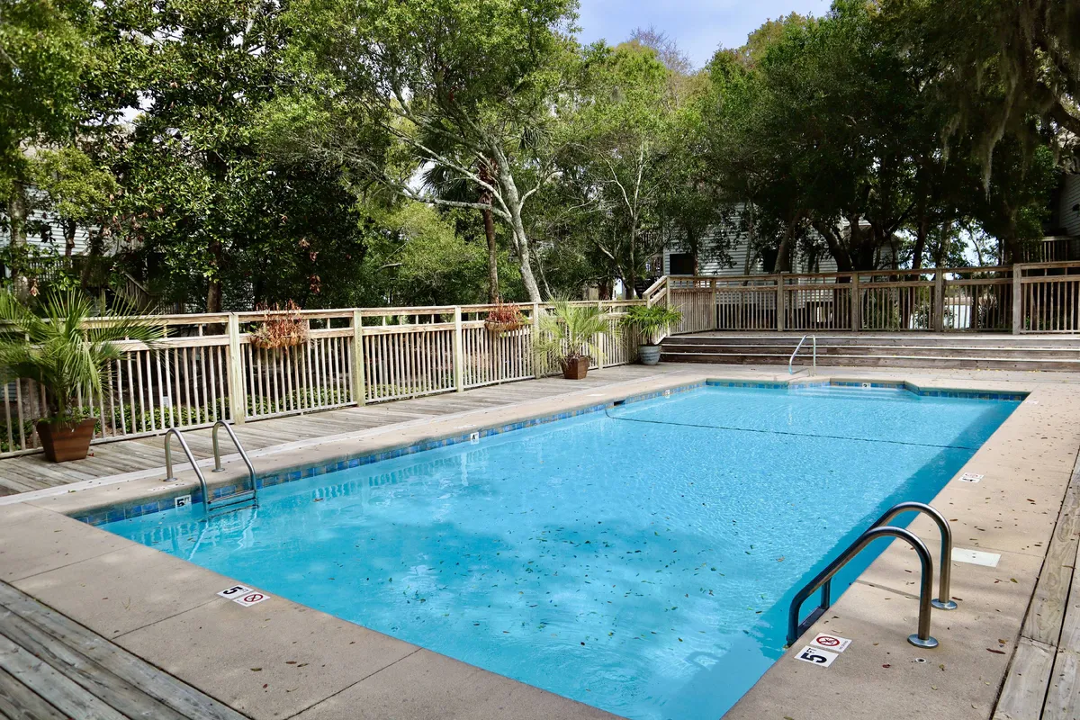 A serene exterior shot of the community saltwater pool surrounded by greenery, a wooden deck, and comfortable poolside furniture, evoking a sense of relaxation and social gathering.