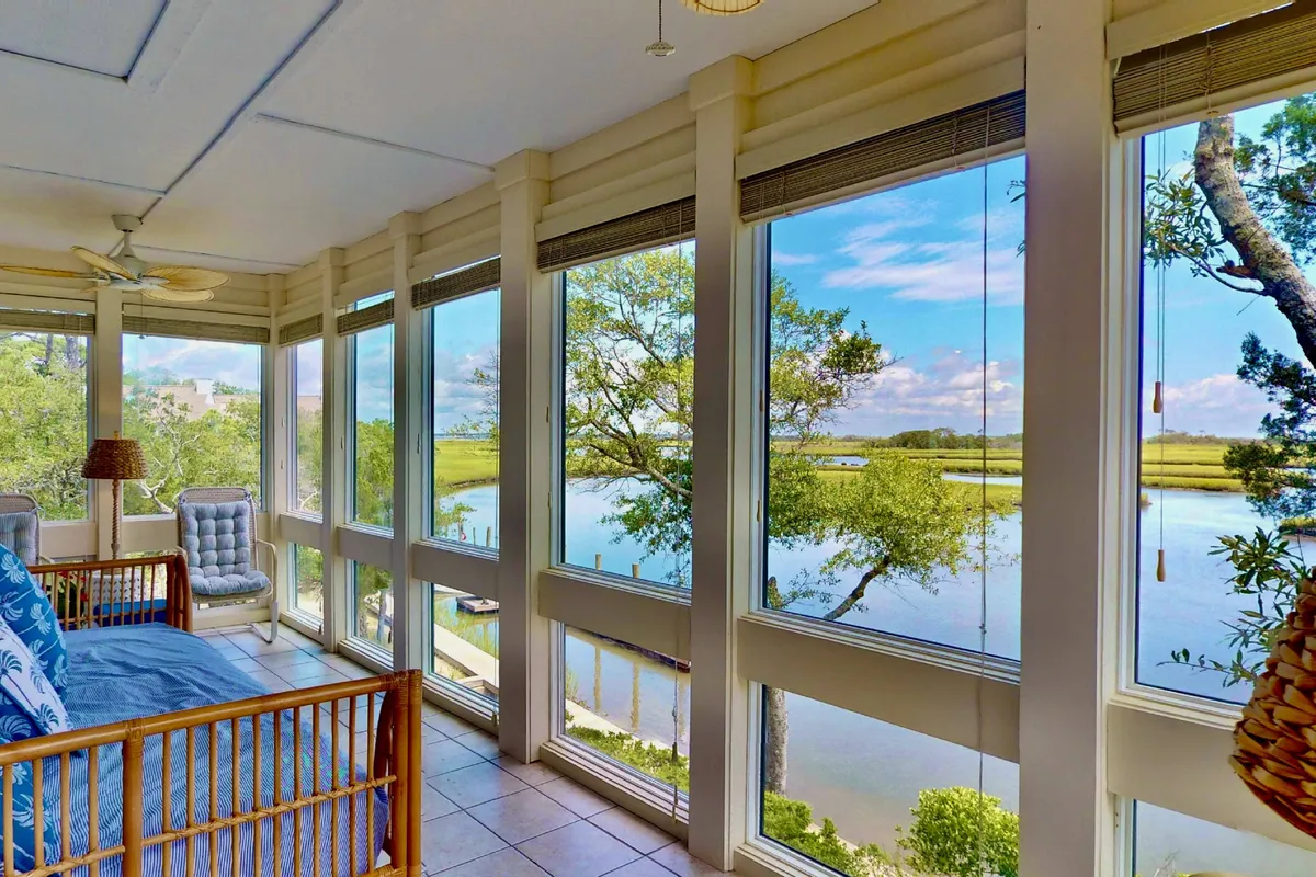 A tranquil living space oriented around large windows overlooking the water. Comfortable seating and stylish decorative elements, including a lamp and houseplants, set the stage for relaxed mornings or evenings spent enjoying the natural surroundings. The space is perfectly set up for group conversation or quiet reading, with direct sightlines to the water beyond.