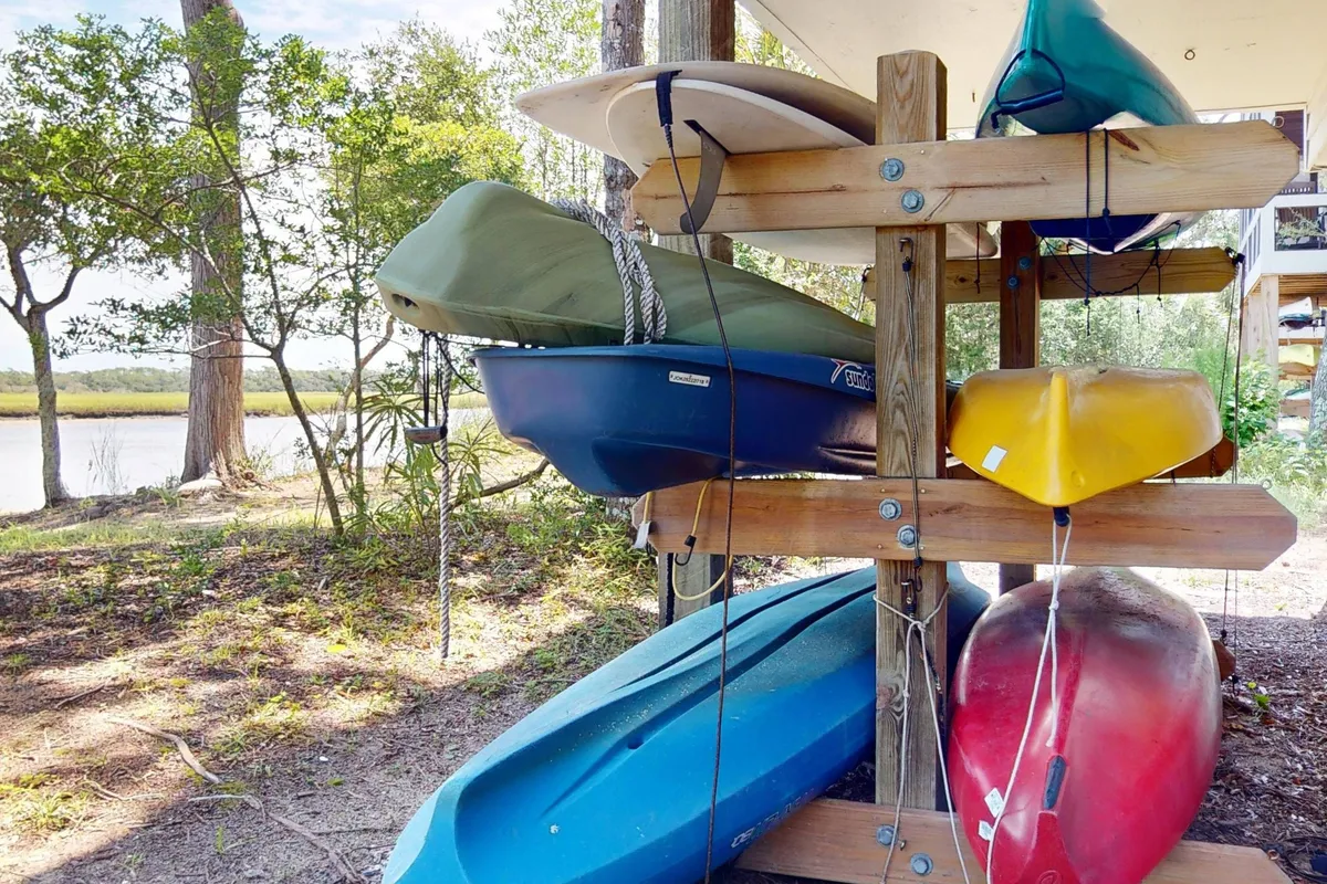 This exterior image showcases a stack of kayaks set against a scenic water view and surrounded by lush trees, suggesting immediate access to kayaking adventures in a tranquil environment.