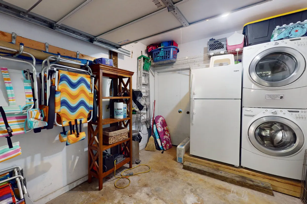 A neatly organized laundry area featuring a stacked washer and dryer, open wooden shelving with colorful household items, and laundry baskets. The space is practical and tidy, reflecting thoughtful amenities for guest comfort.