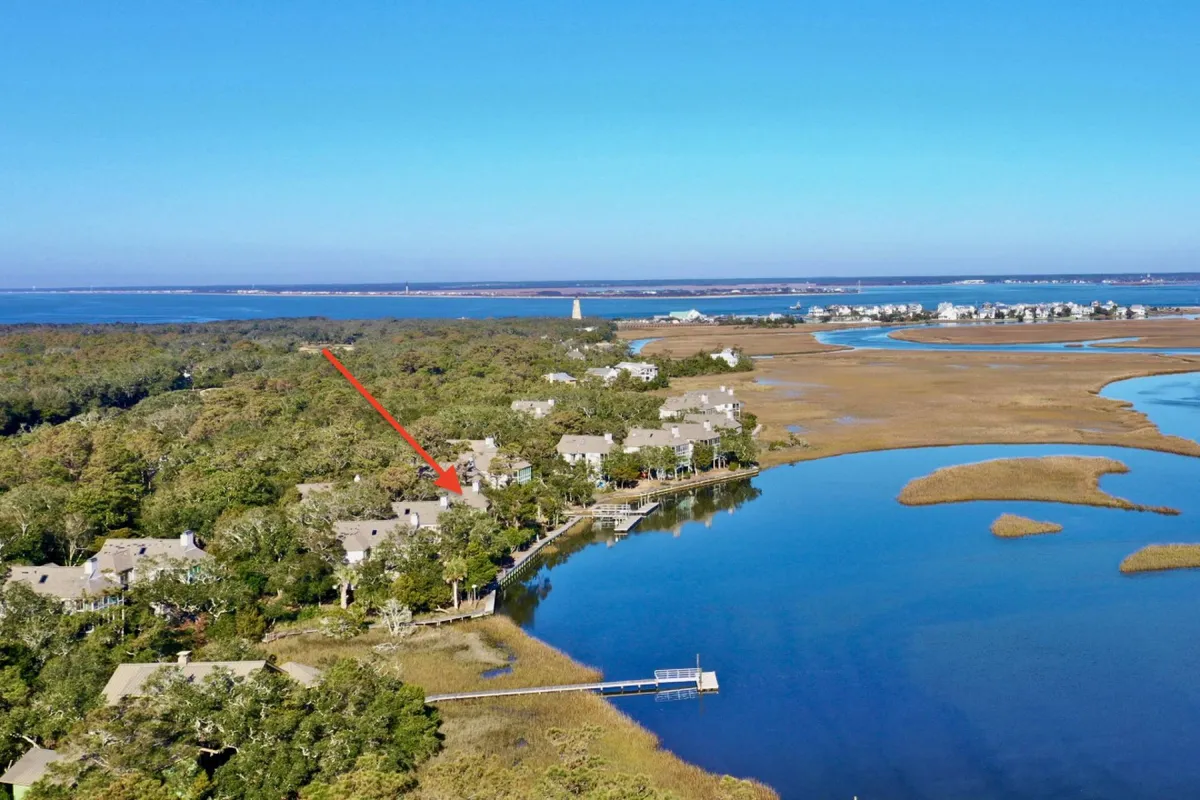 A broad waterfront scene featuring tranquil water, lush surrounding greenery, a distant lighthouse, and neighboring houses. The view captures the peaceful outdoor ambiance and hints at opportunities for water-based recreation.